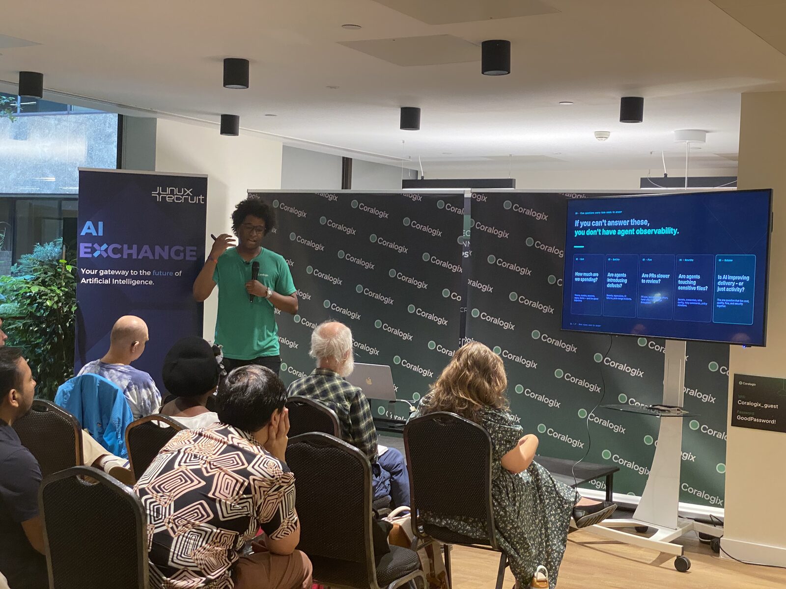 A speaker mid-talk beside a slide reading “If you can’t answer these, you don’t have agent observability”, listing five questions on cost, quality, flow, security and outcome.