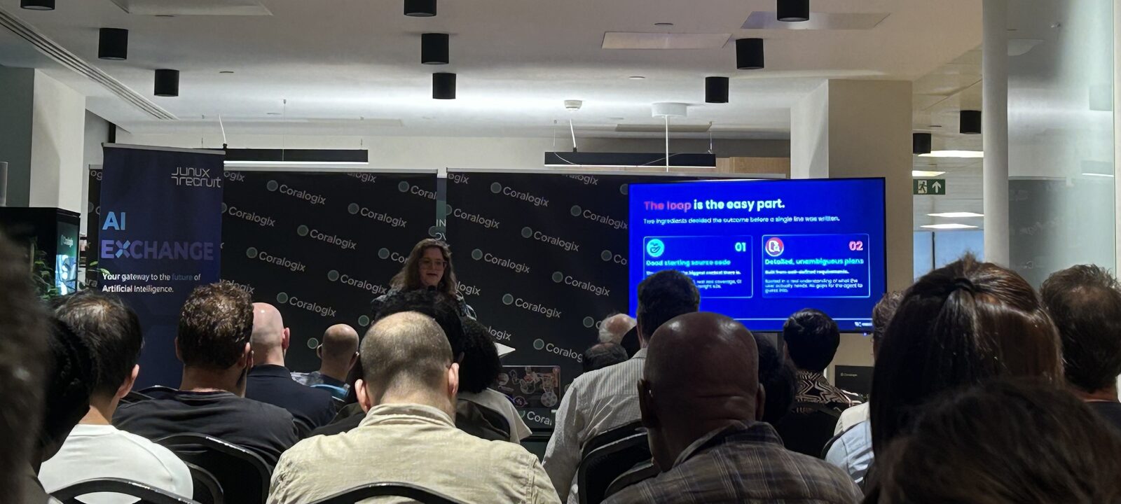 A full room at AI Exchange @ Coralogix, the audience seated in rows facing a speaker and a projected slide.